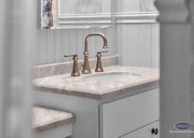 Bathroom vanity with light stone countertop, undermount sink, and brushed brass faucet