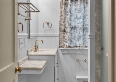 Narrow bathroom layout with vanity, walk-in shower, beadboard walls, and patterned shower curtain