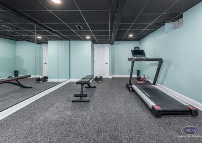 Home gym with treadmill, workout bench, mirrored wall, and rubber flooring in this finished Voorhees basement remodel.