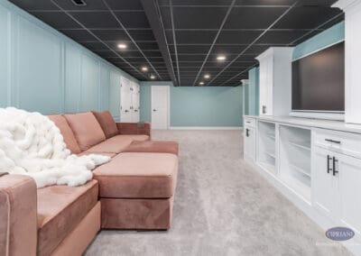 Finished basement lounge with custom built-in media cabinet, teal wall paneling, and sectional seating in this Voorhees basement remodel.