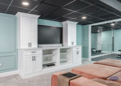 Custom built-in basement media wall with white shaker cabinetry and glass-enclosed home gym in this Voorhees basement remodel.