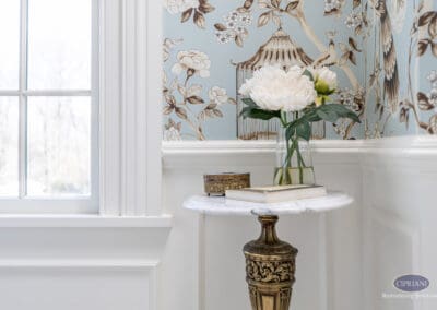 Elegant powder room vignette with marble pedestal table, floral arrangement, and blue chinoiserie wallpaper