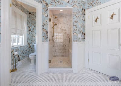 Glass walk-in shower with brass fixtures and blue chinoiserie wallpaper in Mullica Hill bathroom remodel